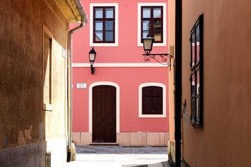 Fototapeta na wymiar narrow alley way in European town with yellow and pink stucco walls and facades. old style wood windows. travel and tourism concept. classic european residential architecture. sconce street lighting.