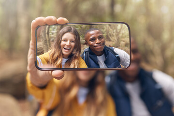 Happy couple taking a selfie on a phone while in nature on a romantic date in the forest. Multiracial, love and traveling man and woman taking picture with smartphone camera after hiking in the woods