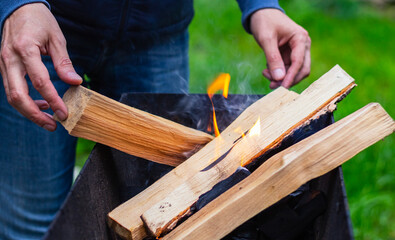 Close-up of Man throws firewood into brazier burns wooden logs. Preparing for picnic selective focus