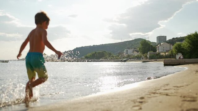 Slow motion video of a little boy running along the seashore splashing water with his feet. A happy child on vacation at sunset is injured. High quality 4k footage