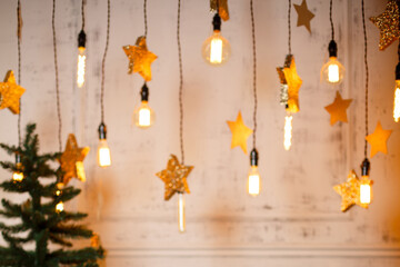 golden stars and bulbs glowing with yellow light hang against background of an old painted wall. Christmas and New Year background, backdrop. Blurred image, selective focus