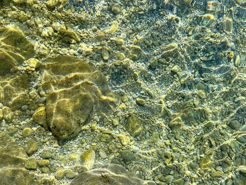 Sea transparent water with smooth stones, pebbles and sand at the bottom of the sea.