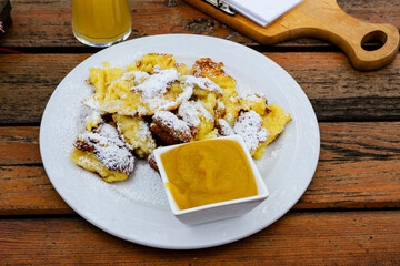 A top view of kaiserschmarrn on a white plate served traditionally with apple puree and powdered sugar on a rustic wooden table. Authentic recipe of austrian torn pancake kaiserschmarrn.
