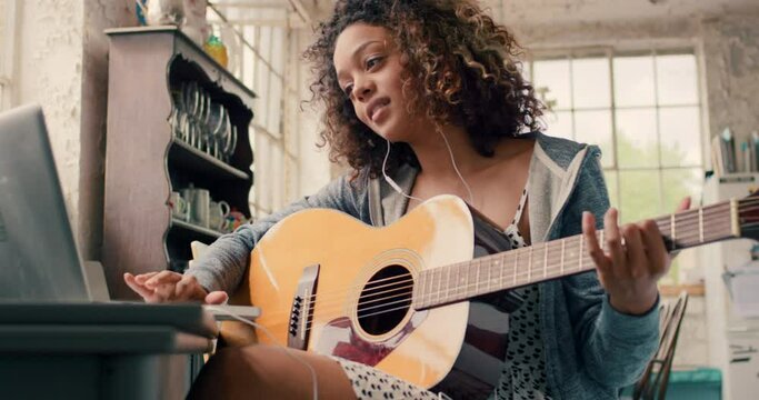 Black woman playing the guitar while watching a music tutorial on a laptop at home, relax and having fun. Young carefree African American female practice her hobby, follow online instructions
