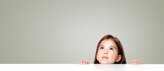 Cute little child girl looking up on the desk at school. - 527500152