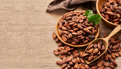 cocoa seed or cacao beans and green leaf or leaves in wood scoop and plate in wooden table background