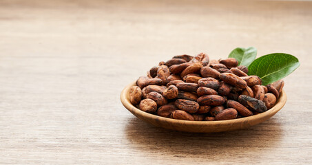 cocoa seed or cacao beans and green leaf or leaves in wood plate on wooden table background                                                                                                    