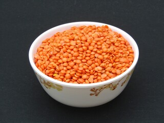 Red lentils in a bowl on black background 