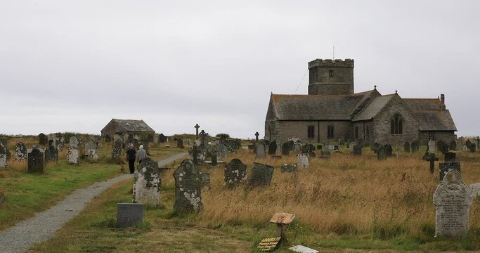 The Saint Materiana's Church in Tintagel with a couple walking through the churchyard path with a dog on a gloomy dull day in Cornwall.