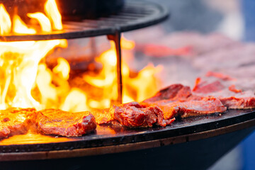 Street food concept. Chef cook prepares Beef steak is fried on open fire outdoor grill in shape of circle