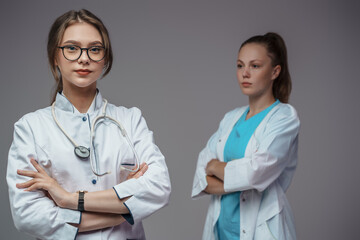 Fototapeta premium Portrait of two professional nurses dressed in labcoats posing against gray background.
