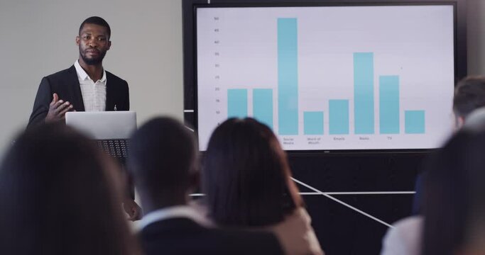 Business, conference and presentation of a black man at the office speaking to employee workers on a podium. Successful African corporate male presenting graph or chart for company goals in workshop.