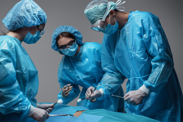 Portrait of three surgeons dressed in surgical uniform treating injured patient against grey...