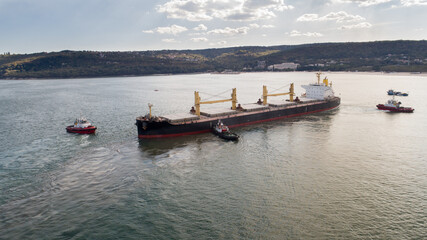 Aerial view of tug boats assisting big cargo ship. Large cargo ship enters the port escorted by tugboats.