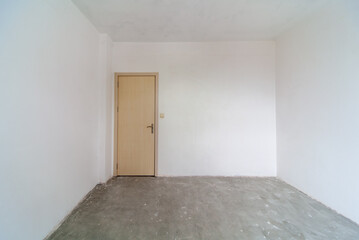 Closed wooden door in empty room, white walls. New empty room under construction. Interior renovation.