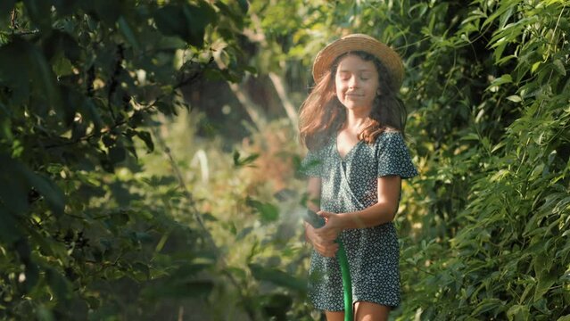 A cute little girl in a straw hat is hosing down the garden. Slow motion. Concept of organic gardening and farming.