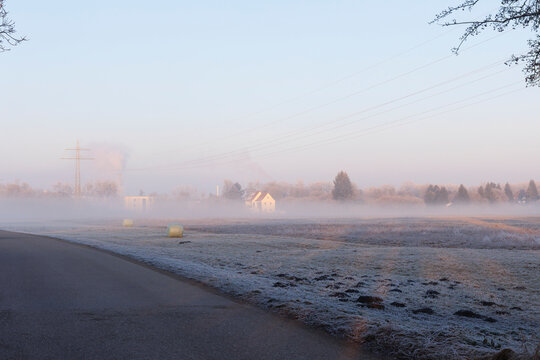 A house on the edge of the forest on a foggy winter morning in a frosted meadow