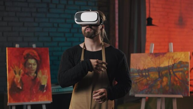 Caucasian talented painter in VR headset standing at workshop and gesturing with hands in air. Inspired art master using modern technology for experience augmented reality.