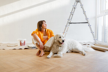 Young woman sits with her dog in room while making repairment in apartment. Repair and house...