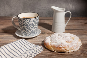 Desayuno con ensaimada (enseimada) de Mallorca y café con leche sobre una mesa de madera.