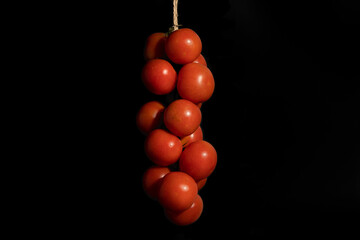 Ristra de tomates de rama (tomate de ramellet o remellet) sobre fondo negro. Variedad de tomate muy...
