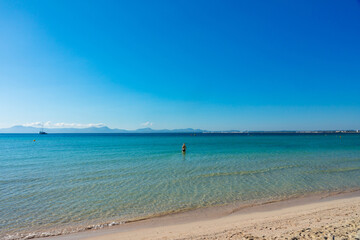 Playa de Alcudia (mallorca): mujer entrando en la tranquilidad de las aguas cristalinas y turquesas de la playa.