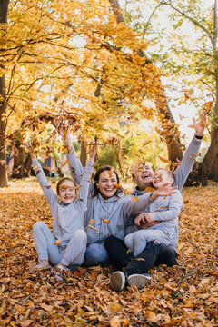 Portrait of a family taking group photos while happily throwing dry leaves of different colours in the air, spending time together during autumn. Family