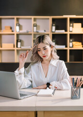 Woman who is tired and overthinking from working with tablet and laptop at modern office..