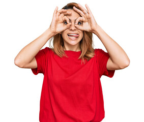 Hispanic young woman wearing casual red t shirt doing ok gesture like binoculars sticking tongue out, eyes looking through fingers. crazy expression.