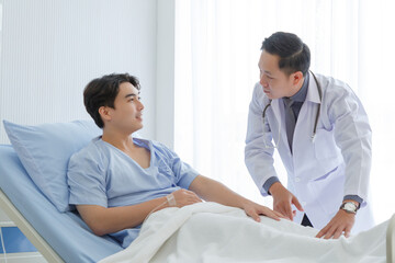 Senior doctor and young male patient who lie on the bed while checking symptom, consult and explain in hospital wards.