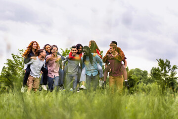 Group of multiethnic young cheerful people walking together and playing piggyback in the countryside - happy friends having fun gathering in the weekend - trust, unity and diversity lifestyle concept