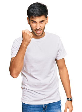 Young handsome man wearing casual white tshirt angry and mad raising fist frustrated and furious while shouting with anger. rage and aggressive concept.