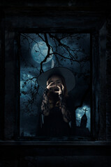 Fototapeta na wymiar Scary halloween witch standing in old damaged wood window with wall over cross, church, birds, dead tree and spooky cloudy sky, Halloween mystery concept