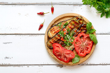 Organic grilled fried eggplant, fresh tomato with greens on a wooden plate on a white background. Top view with copy space. - Powered by Adobe