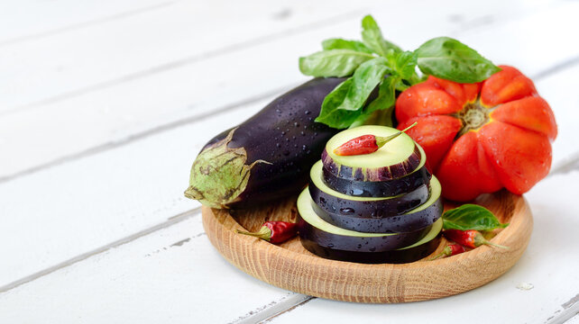 Eggplant, tomato and fresh basil on a wooden plate on a white background with copy space. Ingredients for the eggplant dish