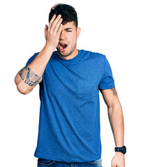 Young hispanic man wearing casual t shirt yawning tired covering half face, eye and mouth with hand. face hurts in pain.