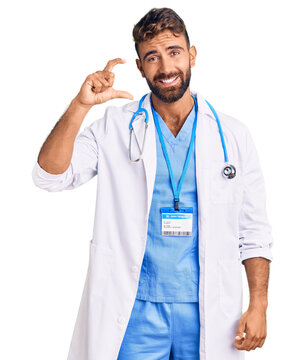 Young hispanic man wearing doctor uniform and stethoscope smiling and confident gesturing with hand doing small size sign with fingers looking and the camera. measure concept.