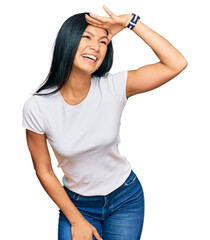 Beautiful hispanic woman wearing casual white tshirt very happy and smiling looking far away with hand over head. searching concept.