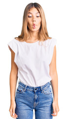 Beautiful caucasian woman with blonde hair wearing casual white tshirt making fish face with lips, crazy and comical gesture. funny expression.