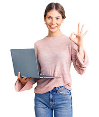 Beautiful caucasian woman with blonde hair working using computer laptop doing ok sign with fingers, smiling friendly gesturing excellent symbol - obrazy, fototapety, plakaty
