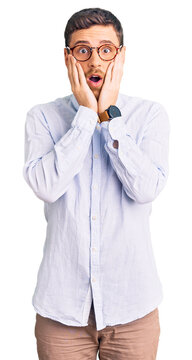 Handsome young man with bear wearing elegant business shirt and glasses afraid and shocked, surprise and amazed expression with hands on face