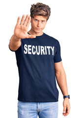 Young handsome man wearing security t shirt doing stop sing with palm of the hand. warning expression with negative and serious gesture on the face.