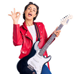 Young beautiful woman playing electric guitar doing ok sign with fingers, smiling friendly...