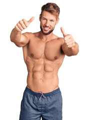 Young caucasian man standing shirtless approving doing positive gesture with hand, thumbs up smiling and happy for success. winner gesture.