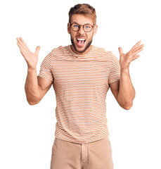 Fototapeta premium Young caucasian man wearing casual clothes and glasses celebrating crazy and amazed for success with arms raised and open eyes screaming excited. winner concept
