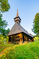 Fototapeta na wymiar Traditional old wooden church with shingle roof and tower in Breb village, Maramures, Romania; Wooden church surrounded by green trees