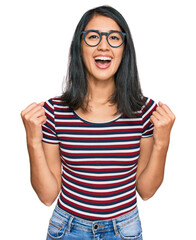 Obraz na płótnie Canvas Beautiful asian young woman wearing casual clothes and glasses celebrating surprised and amazed for success with arms raised and open eyes. winner concept.