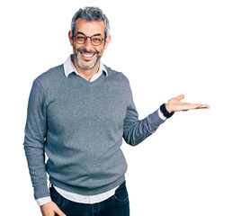 Middle age hispanic with grey hair wearing glasses smiling cheerful presenting and pointing with palm of hand looking at the camera.