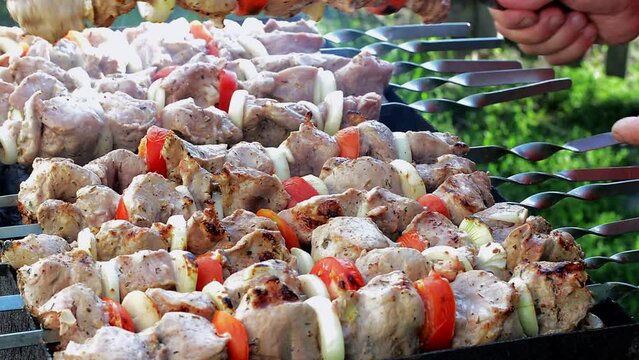 A man's hands rotating the skewers. Shish kebab. Pork or lamb meat pieces being fried on a charcoal grill. Grilling a shashlik during the rest.
