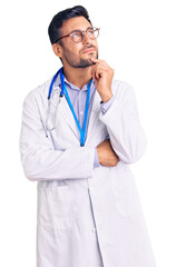 Young hispanic man wearing doctor uniform and stethoscope with hand on chin thinking about question, pensive expression. smiling and thoughtful face. doubt concept.